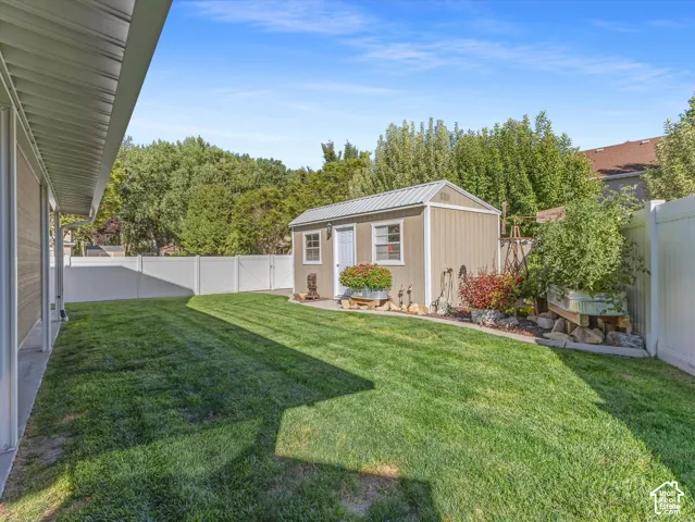Expansive backyard featuring a manicured lawn, a detached storage shed with a metal roof, a white vinyl fence, and mature perimeter trees