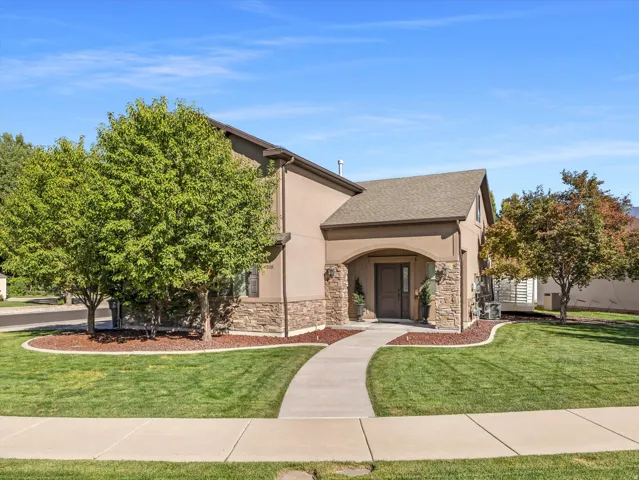 Stucco exterior with stone accents, covered entry, gabled roof, mature landscaping, and a concrete walkway