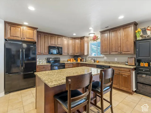 Kitchen featuring a central island with a stone-finish countertop, wood-finish cabinetry, black appliances, and recessed lighting
