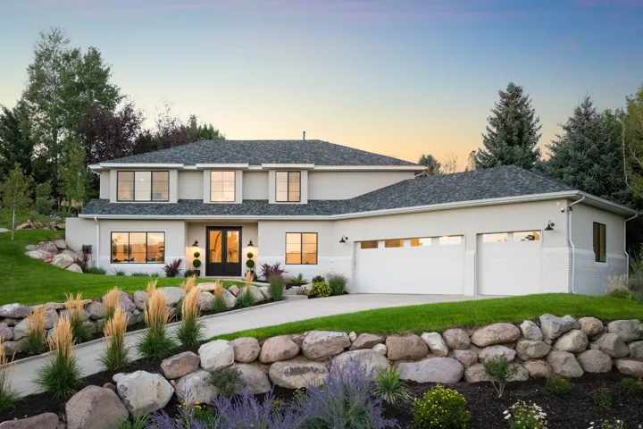 Stucco exterior with a dark shingle roof, integrated two-car garage, and multiple large windows