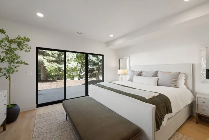 Recessed lighting illuminates the room, featuring wood-finish flooring and a white upholstered bed frame