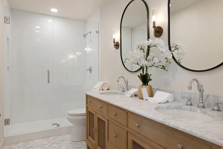 Dual vanity with stone countertop and undermount sinks, wood-finish cabinetry, frameless glass shower enclosure, and tiled shower surround