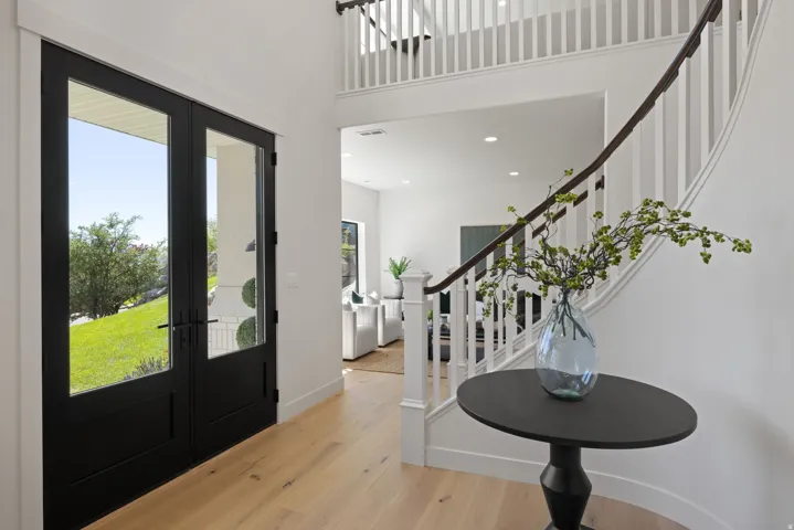Double entry doors with glass panels, light wood-finish flooring, and a curved staircase with white balusters