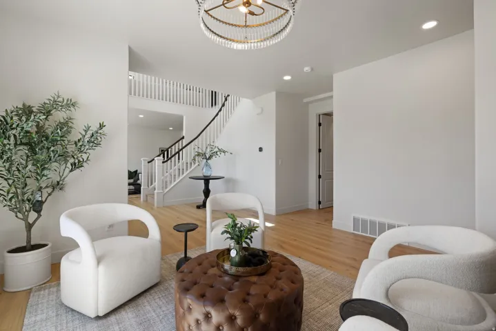 High ceilings with recessed lighting, wood-finish flooring, a grand staircase with white balusters and a dark handrail, a decorative chandelier, and a white paneled door