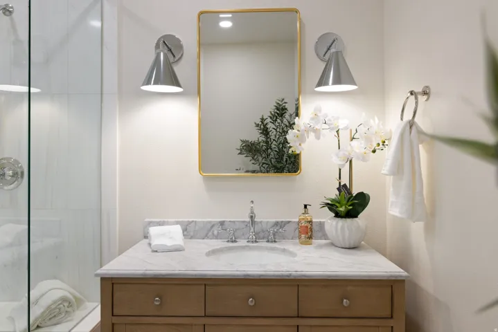Vanity with wood-finish cabinetry, stone countertop with integrated sink, and dual wall-mounted sconces