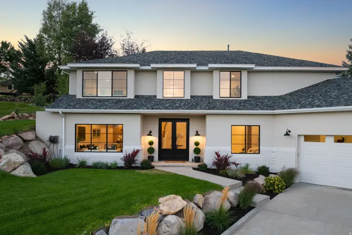 White stucco exterior with black-framed windows, a dark shingle roof, an attached garage, and a concrete driveway