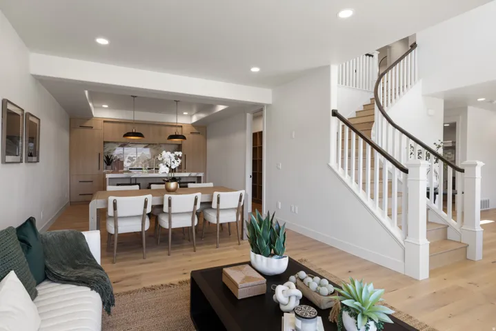 Open-concept living area featuring a curved staircase with white risers and dark wood handrails, recessed lighting, light wood-finish flooring, and a dining area with pendant lighting