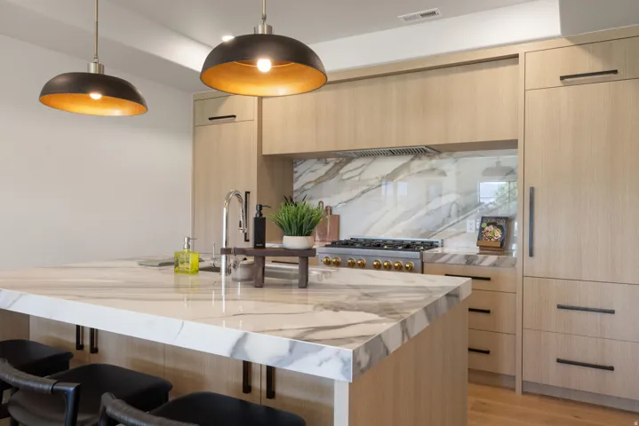 Kitchen featuring a large island with a waterfall edge, integrated sink, and an accenting backsplash