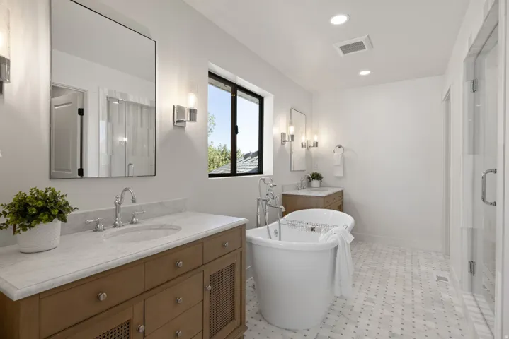 White freestanding soaking tub, wood-finish vanity with stone countertop, and glass-enclosed shower