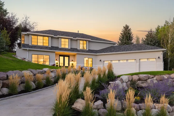 Stucco exterior with a dark shingle roof, dual garage doors, and black-framed windows