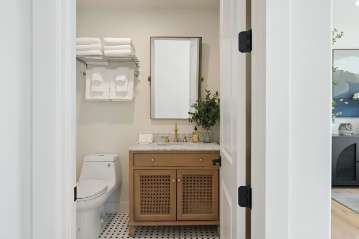 Bathroom featuring a wood-finish vanity with cane-front doors, a polished countertop, and a vanity mirror with a brass frame