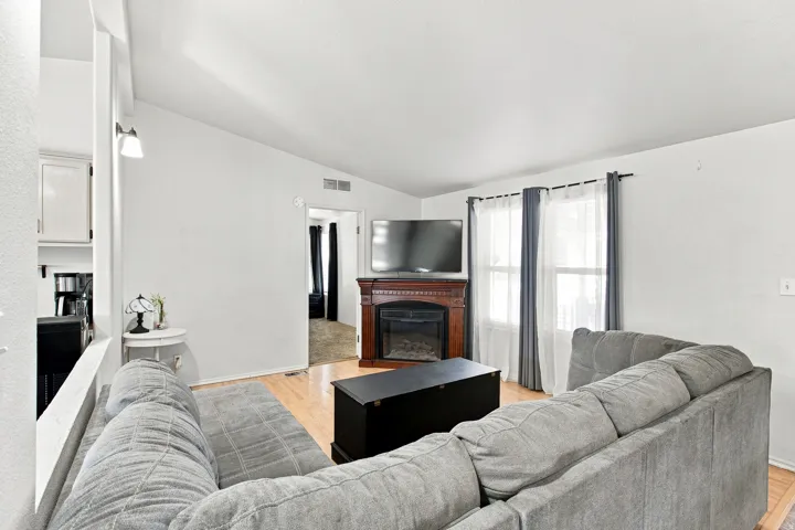 Living area featuring vaulted ceilings, wood-finish flooring, a built-in fireplace with a decorative mantel, and windows with vertical blinds