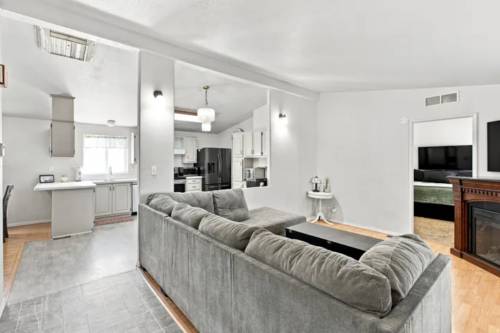 Open-concept living area featuring a fireplace with a wood-finish mantel, wood-finish flooring, and a kitchen with light-toned cabinetry and dark appliances