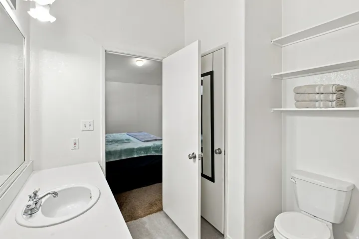 Bathroom featuring a single vanity with an integrated sink, built-in wall shelving, and a white toilet