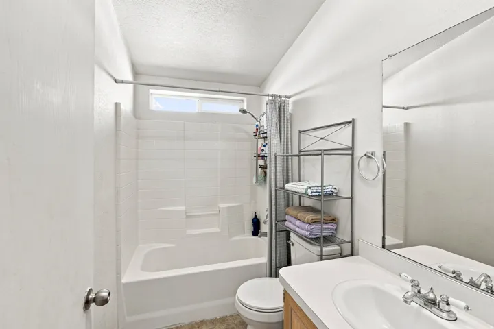 Bathroom featuring a white tub with subway tile surround, single vanity with integrated sink, wood-finish cabinetry, and an upper transom window