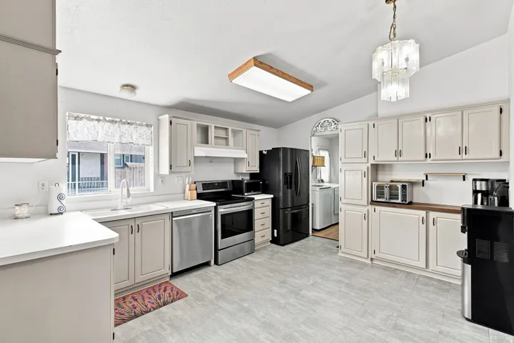 Laminate flooring, perimeter cabinetry, stainless steel dishwasher, stainless steel range, and a glass-paneled chandelier