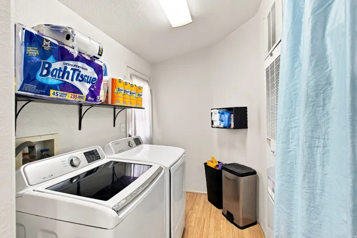 Laundry area featuring wood-finish flooring, wall-mounted shelving, and a wall-mounted storage unit