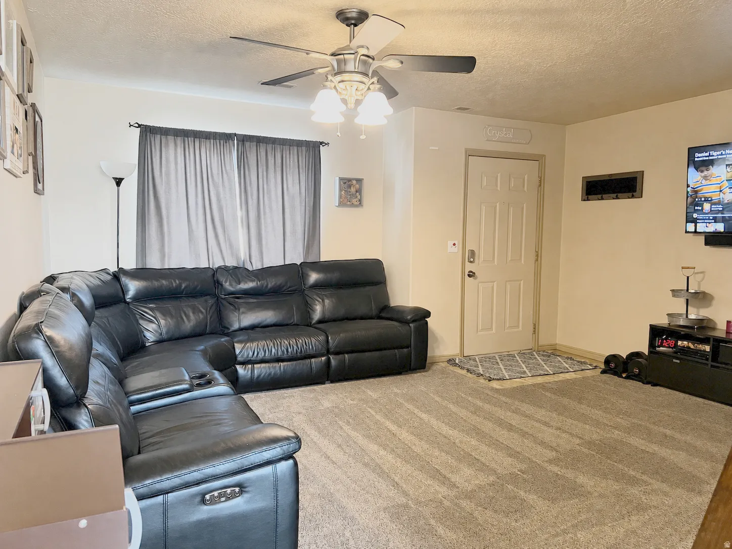 Spacious living room featuring a ceiling fan with integrated lighting, wood-finish flooring throughout, and large windows with soft natural light