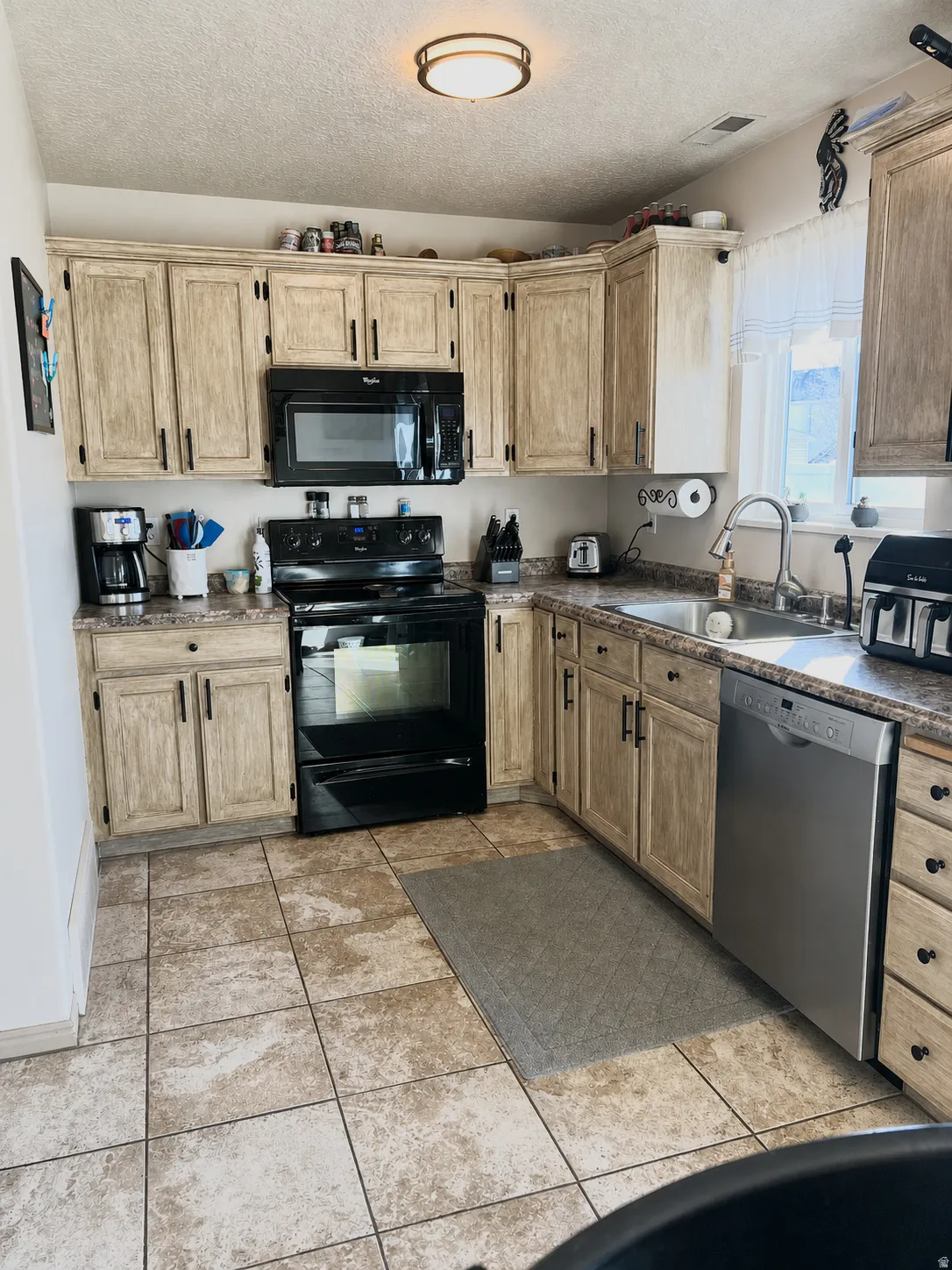 U-shaped kitchen featuring light-toned cabinetry, a black range with an over-the-range microwave, stainless steel dishwasher, and tiled flooring