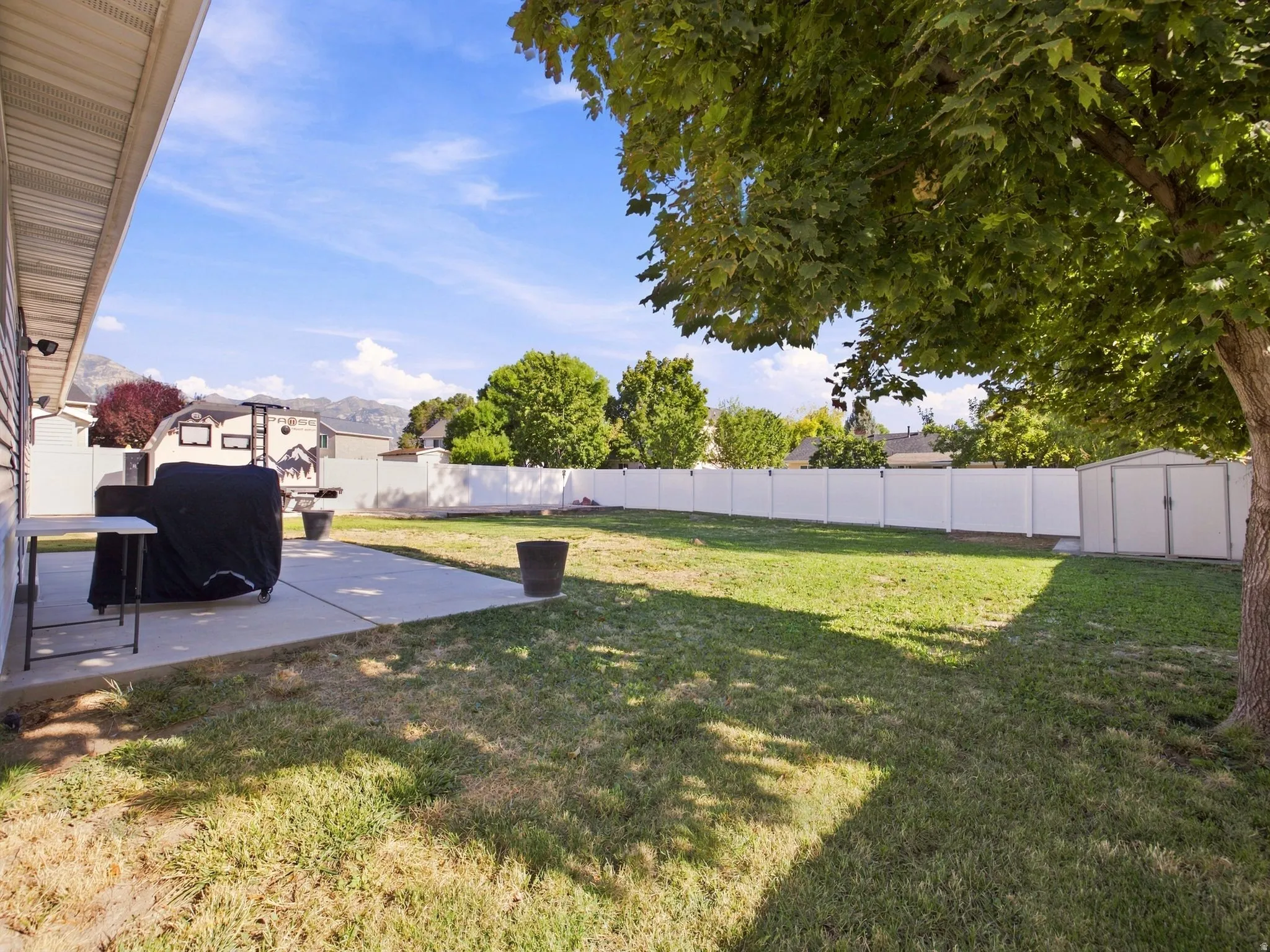 Expansive backyard featuring a concrete patio, mature trees, and a full-height privacy fence