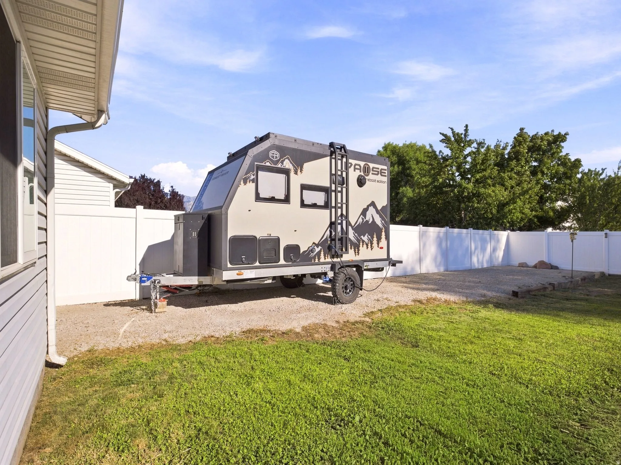 Gravel parking area with a white vinyl fence and a lawn section