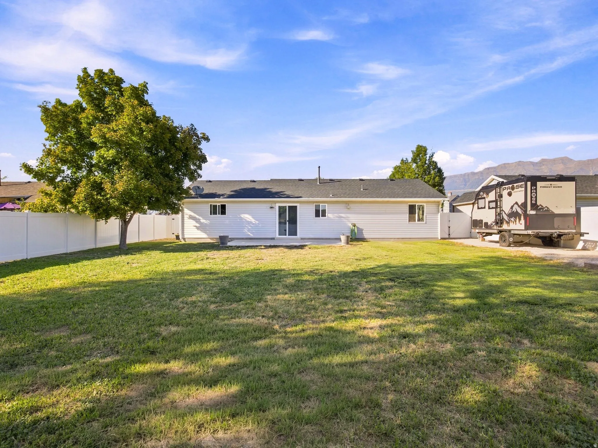 Expansive lawn with a mature tree, white privacy fencing, and mountain backdrop