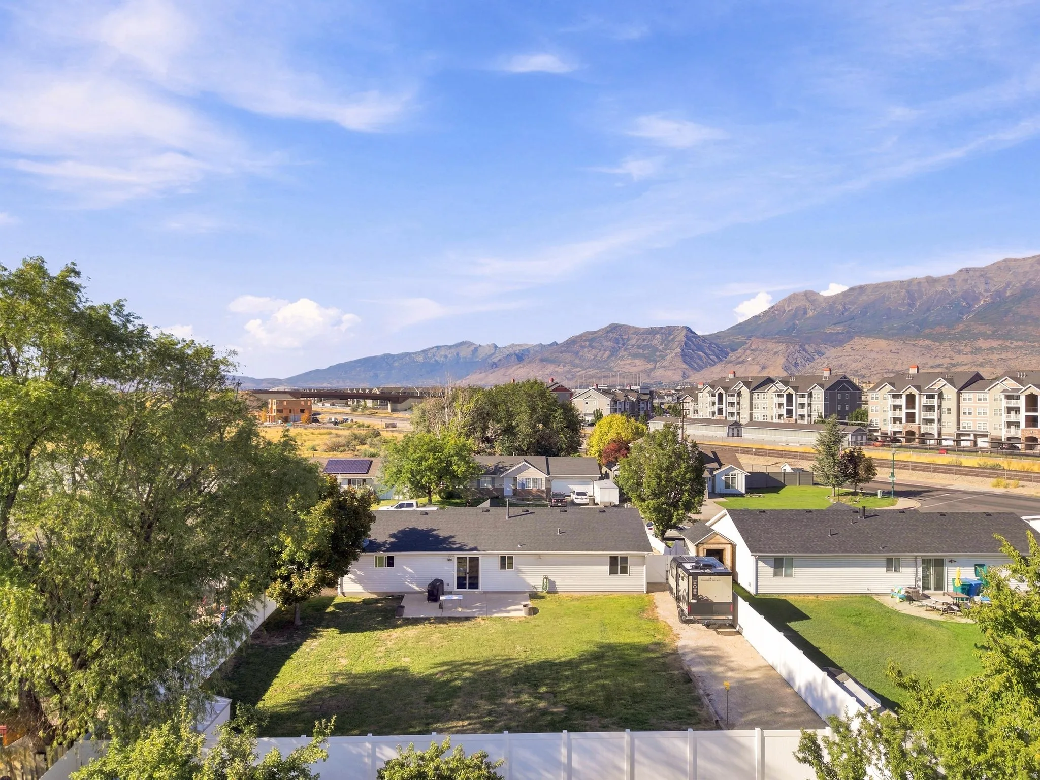 Expansive backyard featuring a manicured lawn, concrete patio, and white privacy fencing