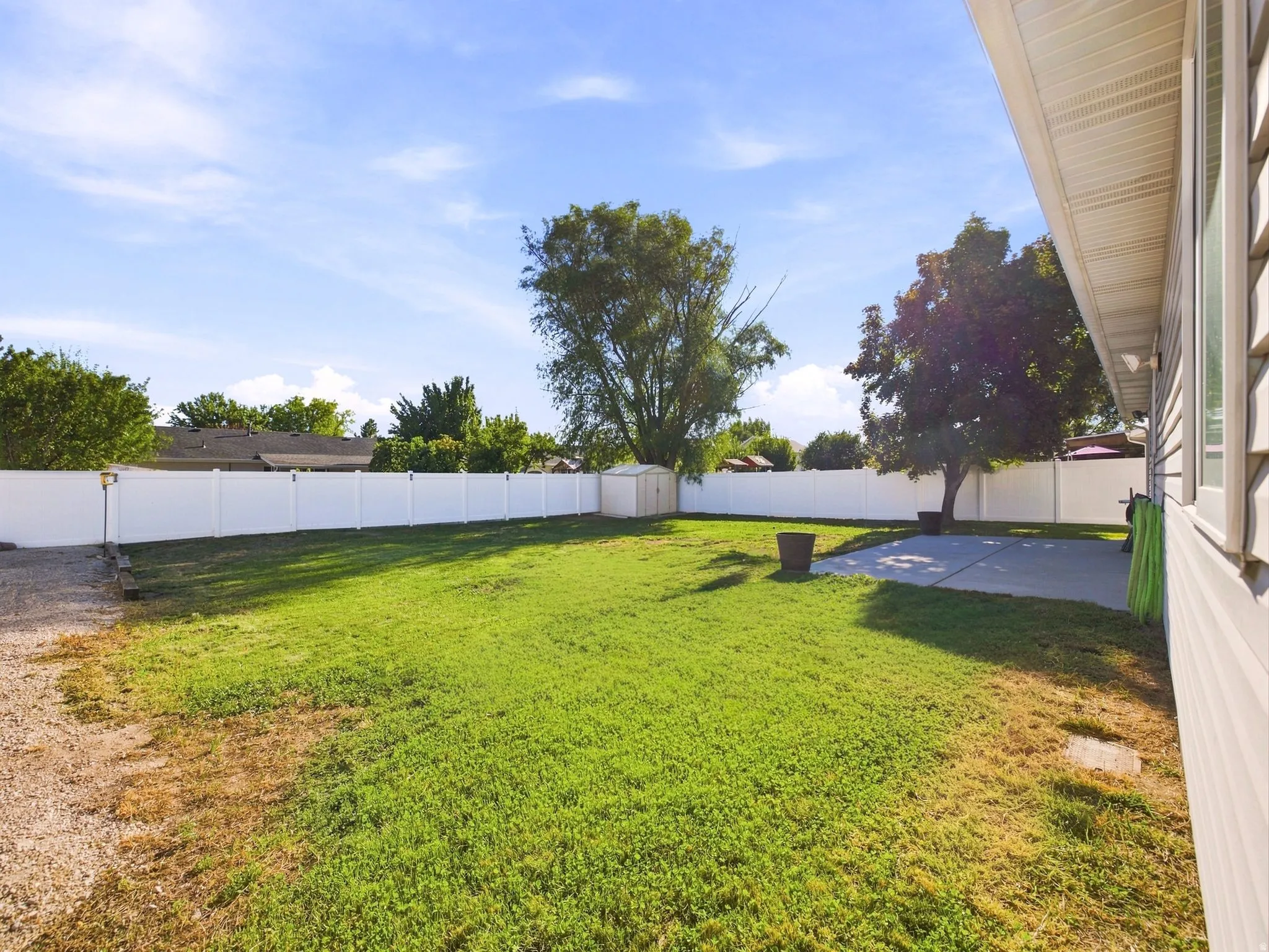 Expansive backyard featuring a lush lawn, white privacy fencing, and a concrete patio