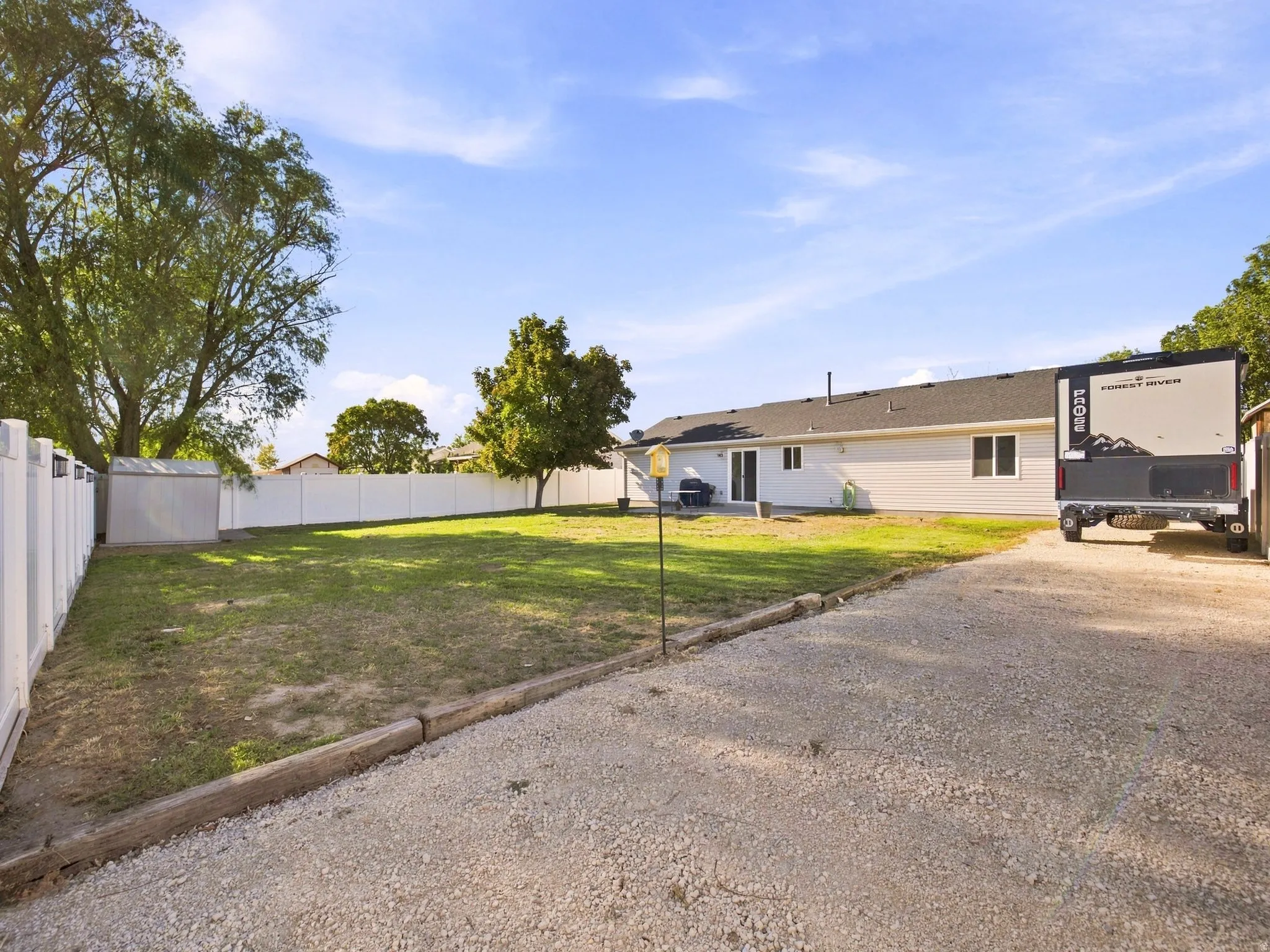 Expansive yard featuring a gravel drive, white privacy fencing, and mature trees
