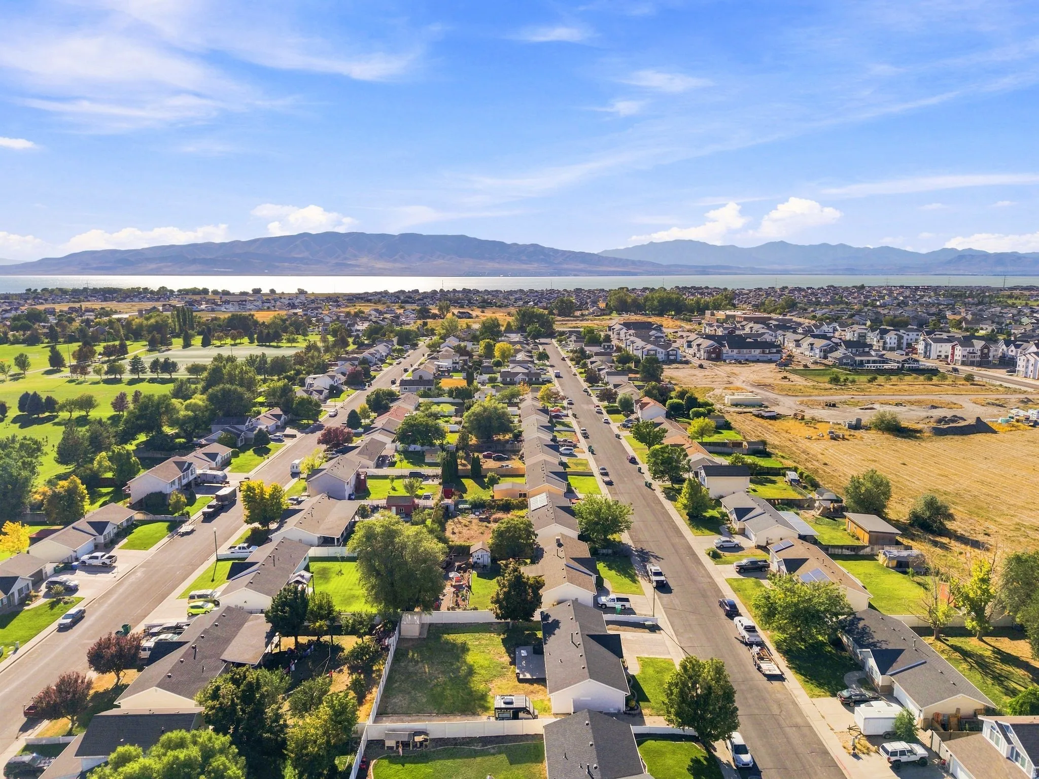 Expansive neighborhood with lush green spaces, residential streets, and distant water and mountain scenery