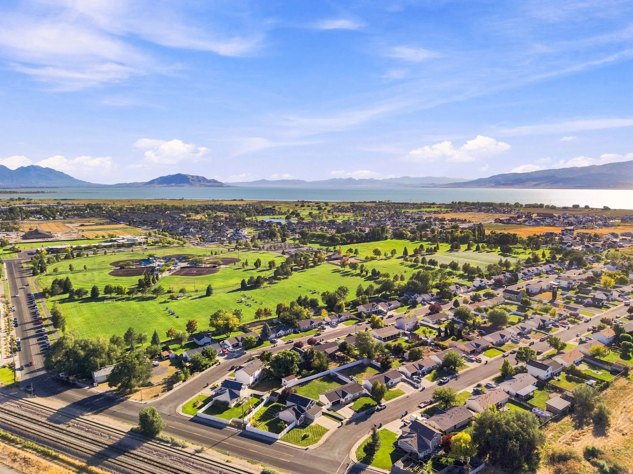 Expansive neighborhood featuring residential properties, recreational green spaces, and a prominent body of water in the background