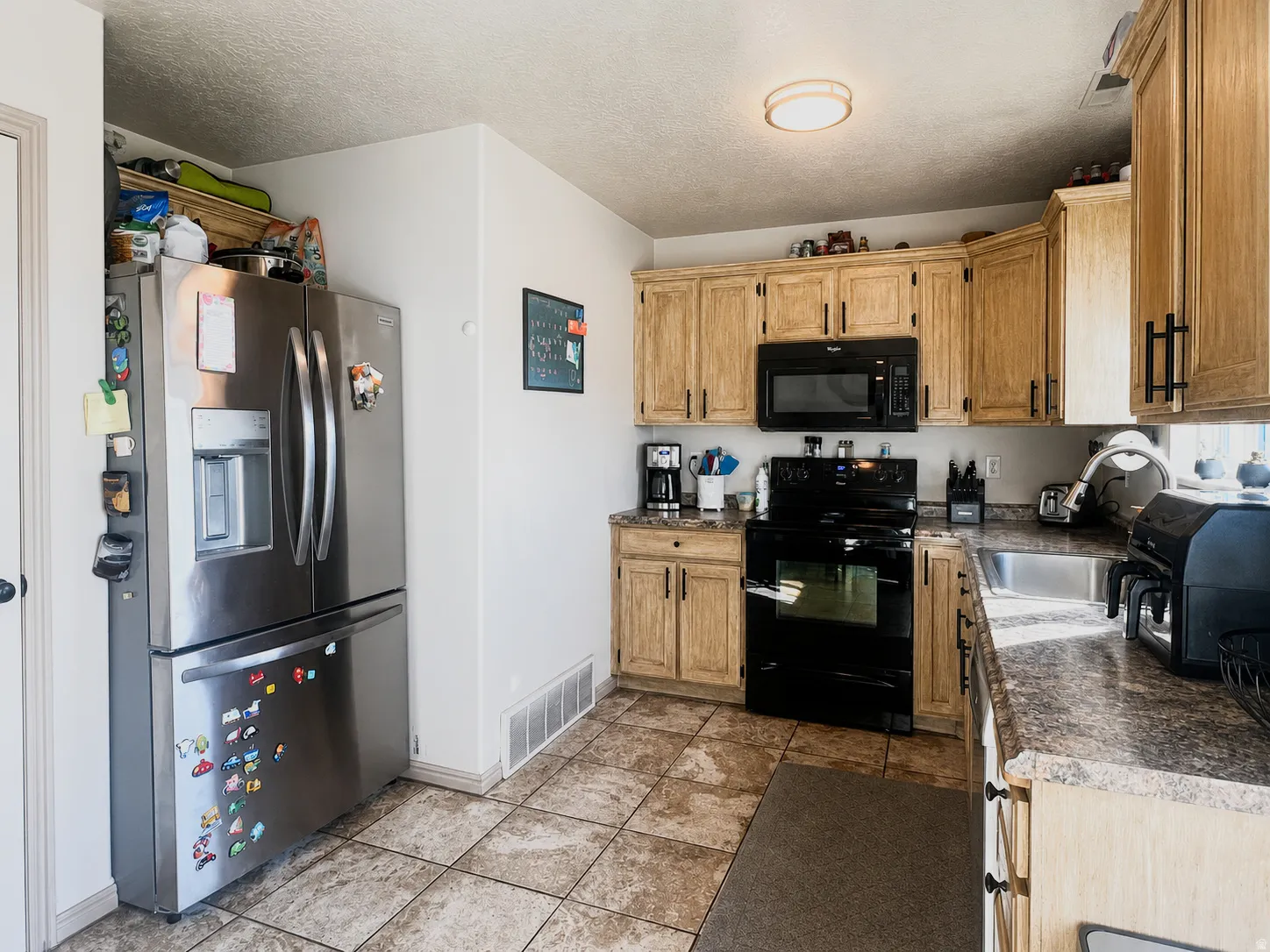 Kitchen featuring tile flooring, wood-finish cabinetry, black appliances, and a stainless steel sink