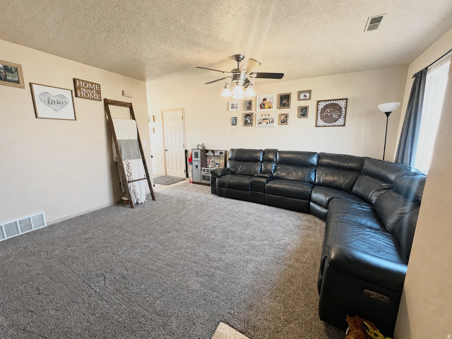 Carpeted living area with light-toned walls and a ceiling fan with light fixture