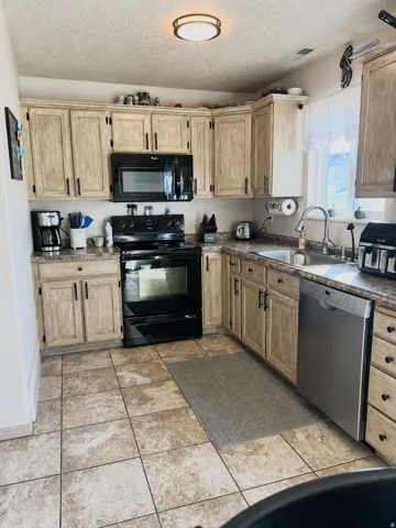 U-shaped kitchen featuring light-toned cabinetry, a black range with an over-the-range microwave, stainless steel dishwasher, and tiled flooring