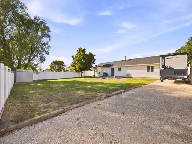 Expansive yard featuring a gravel drive, white privacy fencing, and mature trees