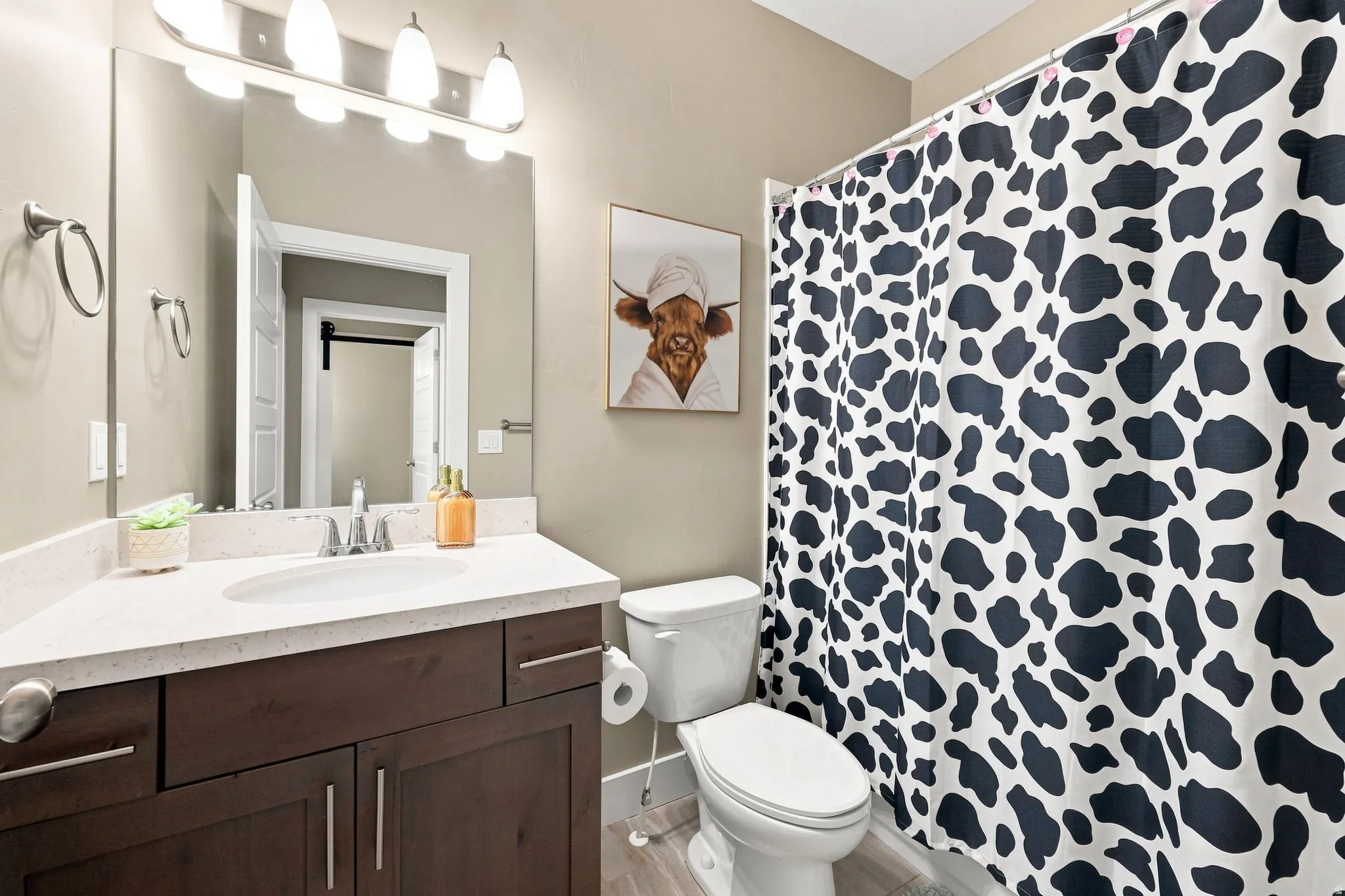 White countertop, wood-finish vanity with ample storage, wall-mounted mirror, and overhead vanity lighting