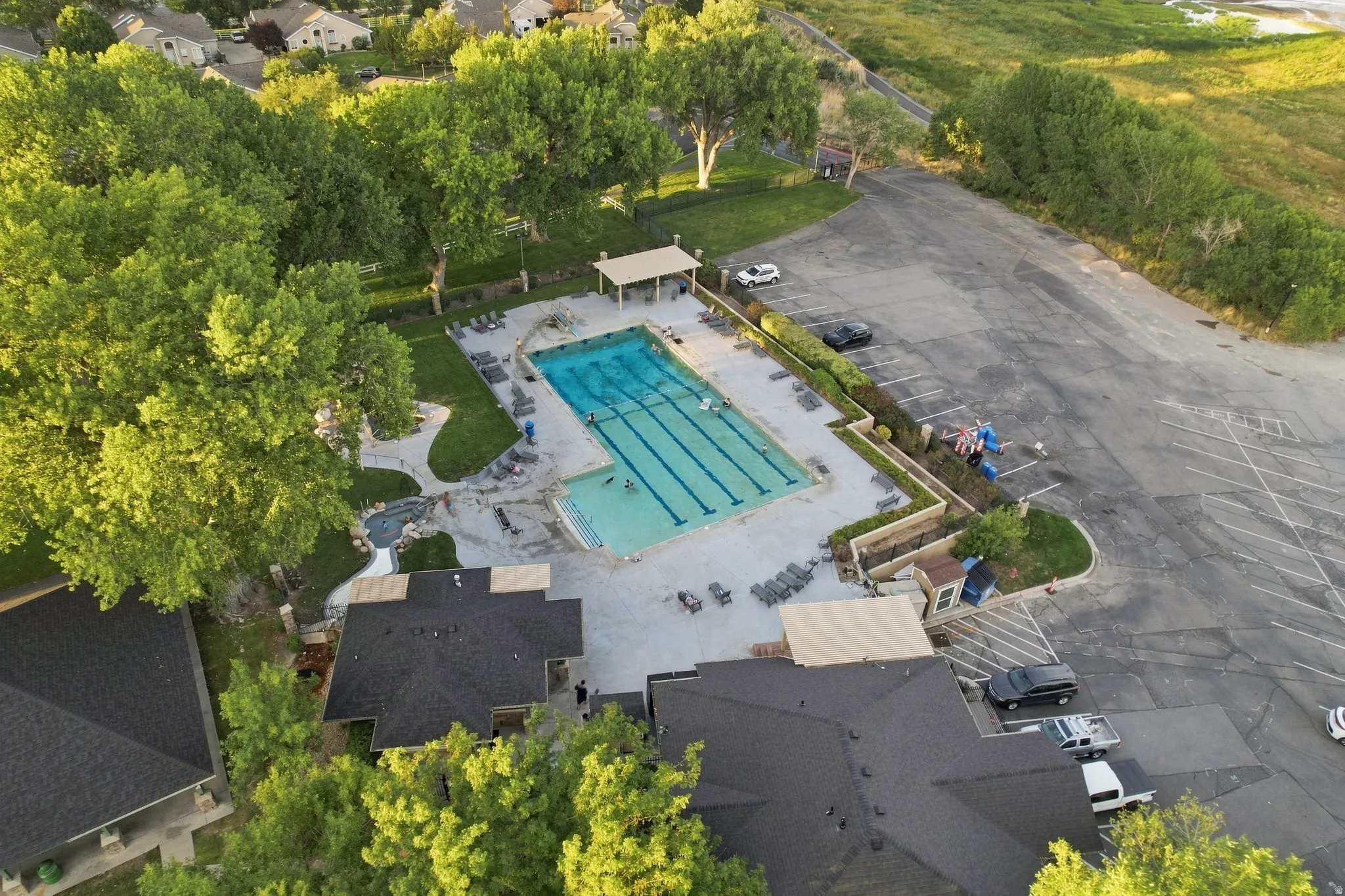 Expansive outdoor swimming pool with lane lines, surrounding hardscaping, adjacent green spaces, and a covered patio area