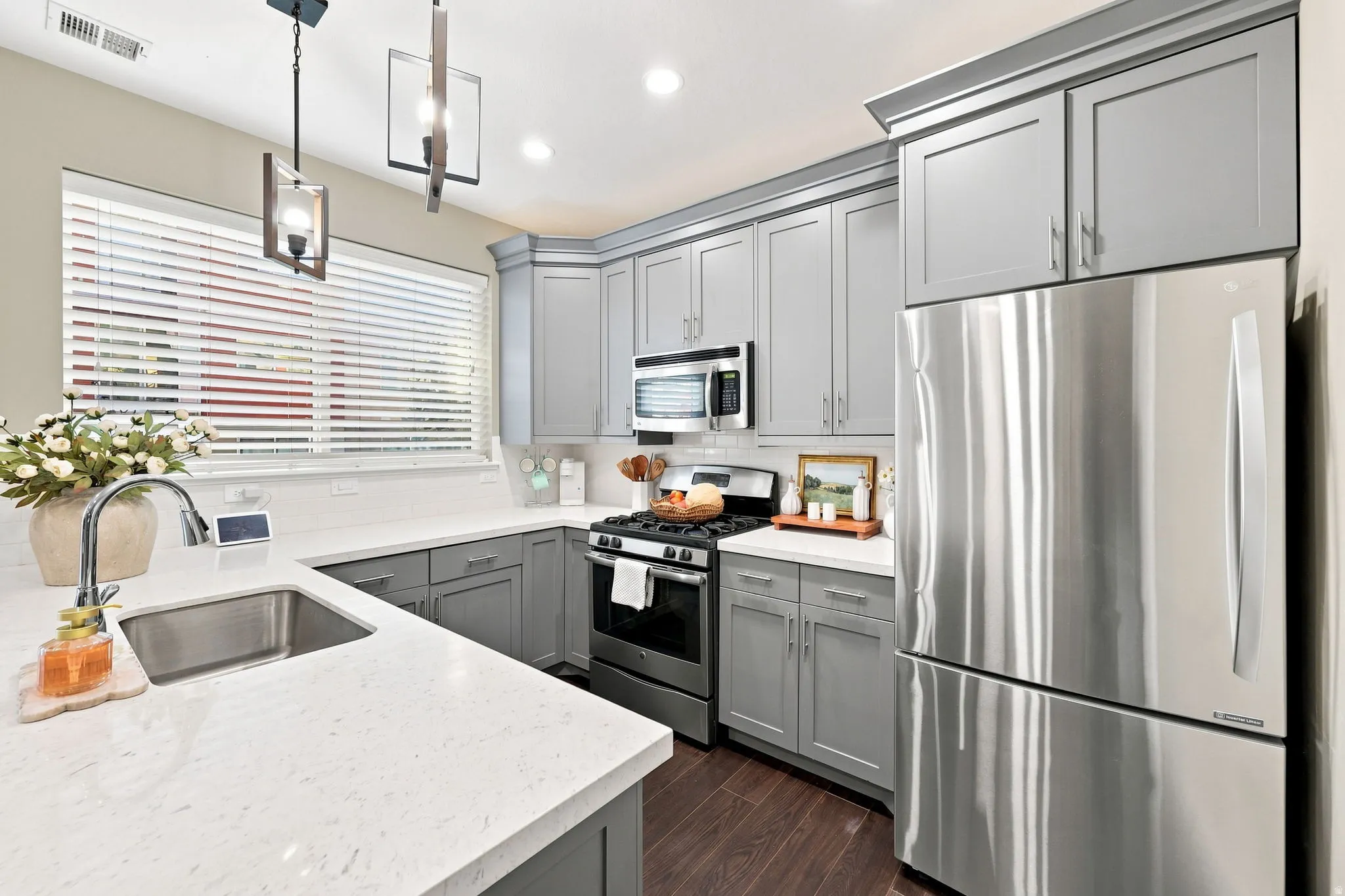 Stainless steel appliances, quartz countertops, gray shaker-style cabinetry, white subway tile backsplash, and wood-finish flooring