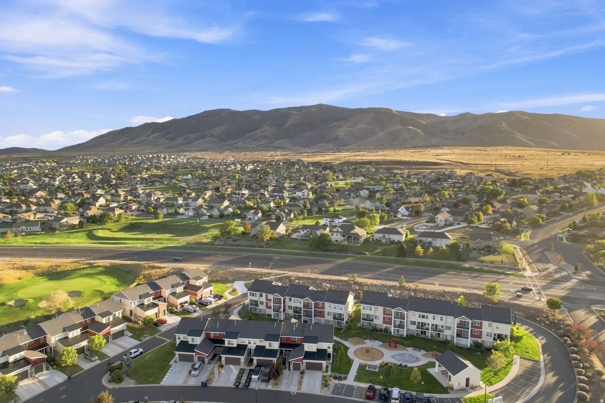 Expansive community with a mountain backdrop, featuring townhomes and multi-story residential buildings, golf course access, and common green spaces
