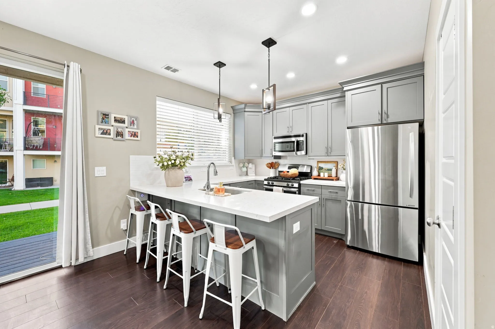 Modern kitchen featuring a large island with white countertop, gray cabinetry, stainless steel appliances, and dark wood-finish flooring
