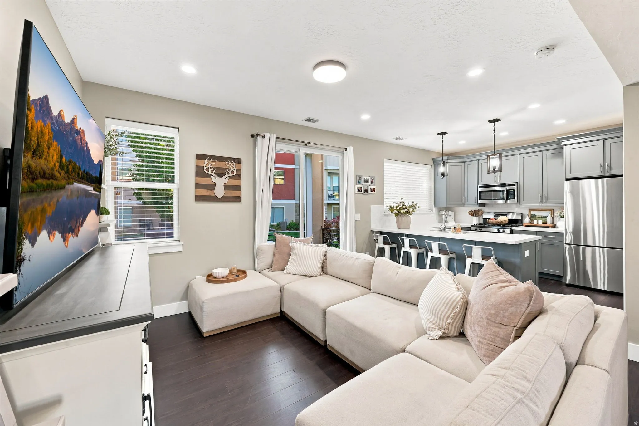 Open-concept living space featuring wood-finish flooring, recessed lighting, and a kitchen with gray cabinetry, an island, and stainless steel appliances