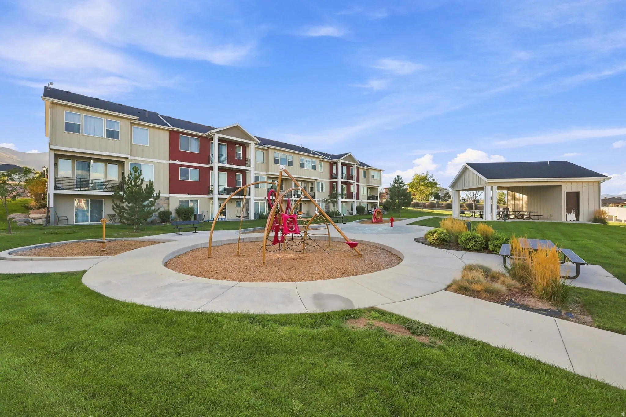 Manicured common grounds featuring a playground, paved walkways, and a covered picnic area