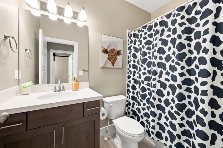 White countertop, wood-finish vanity with ample storage, wall-mounted mirror, and overhead vanity lighting