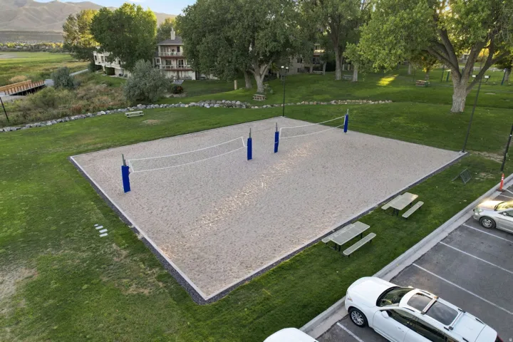 Sand volleyball court with blue net posts, surrounded by green lawn and mature trees