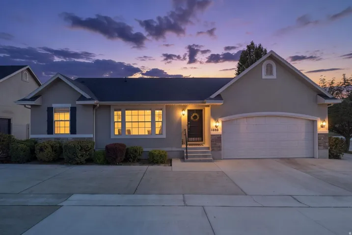 Stucco and stone exterior with an attached garage, featuring a covered entry and professional landscaping