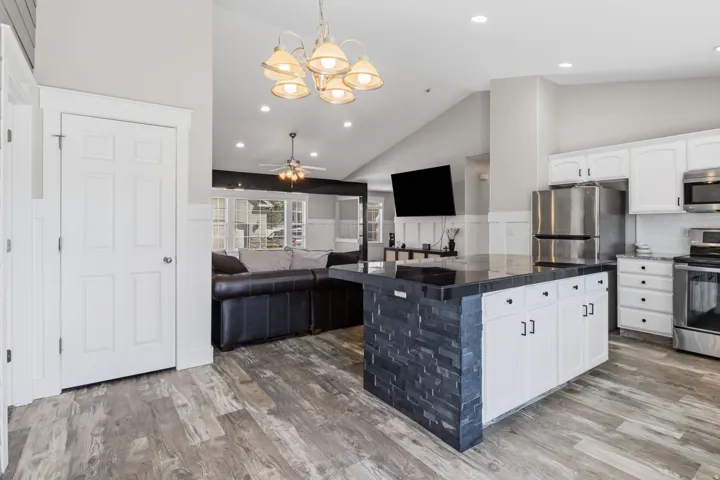 Kitchen featuring white cabinetry, stainless steel appliances, a stone-front island with a dark countertop, and wood-finish flooring