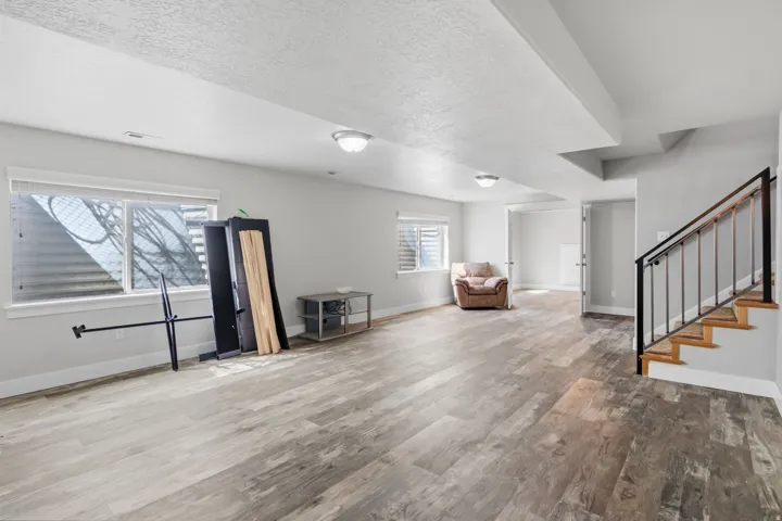 Expansive finished lower level featuring wood-finish flooring, two windows, and a staircase with an iron railing