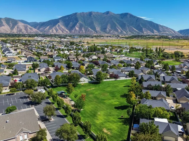 Expansive mountain backdrop with established residential community, abundant mature trees, and a central green space featuring a playground structure