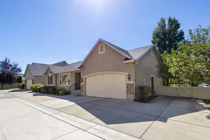 Stucco exterior with stone accents, arched garage door, gabled roofline, and established shrubbery