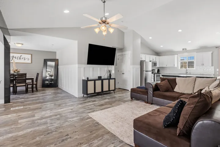 Vaulted ceiling with recessed lighting, wood-finish flooring, white shaker cabinetry, stainless steel appliances, and a tile backsplash